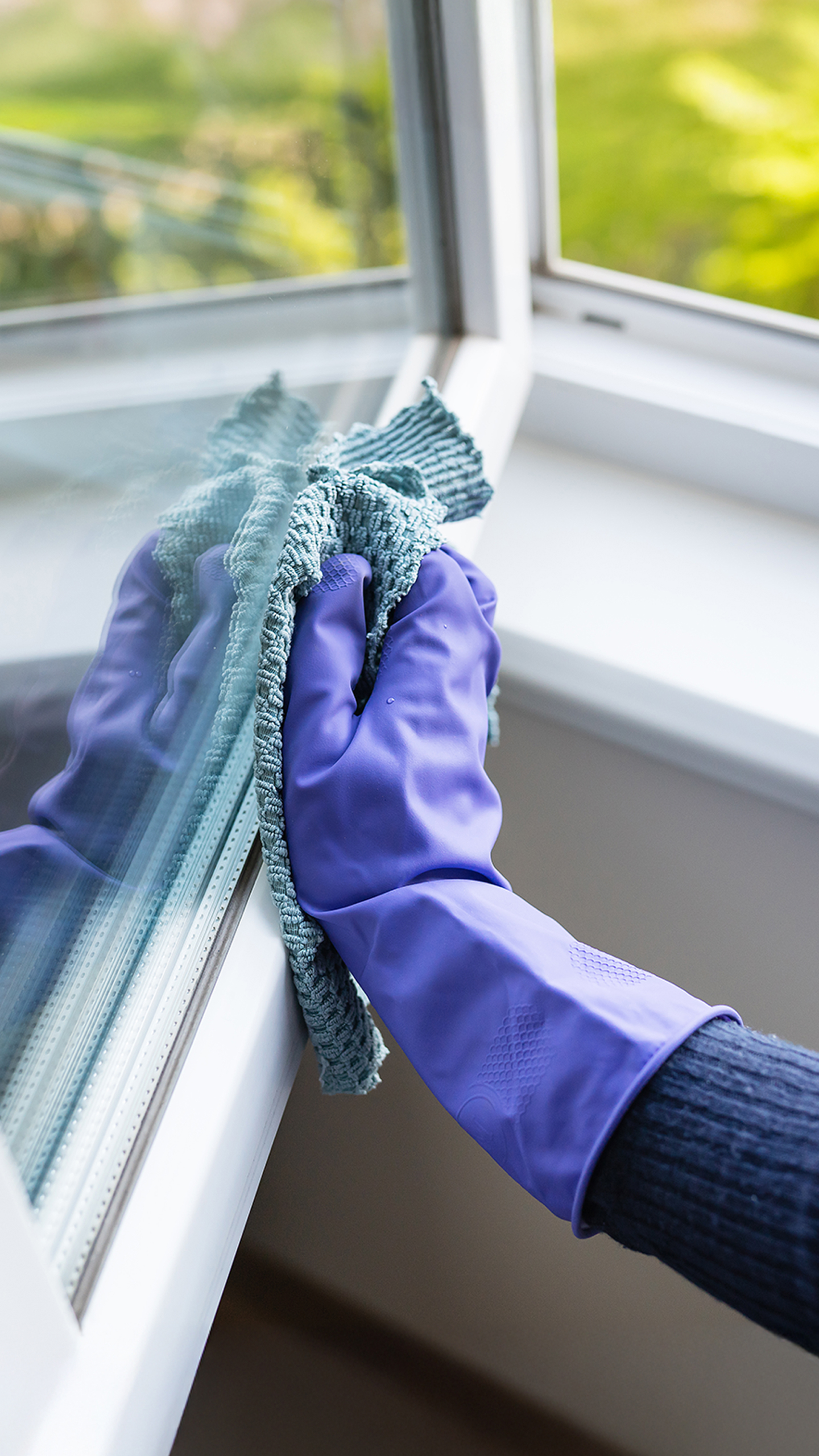 A hand wearing a purple rubber glove is cleaning a window with a blue cloth.